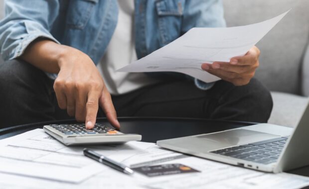 asian young man, male sitting on couch stressed hand calculate expense on table at home