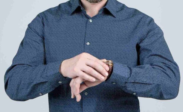 bearded man cropped view in casual shirt check time on watch grey background