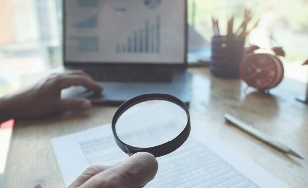 business man using magnifying to review balance sheet annual with using laptop computer to calculating budget