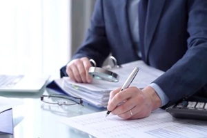 businessman using a calculator and magnifying glass while analyzing financial documents at desk in modern office