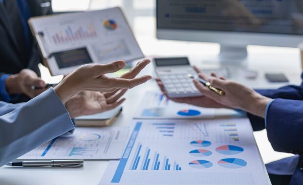 happy young female financial advisor talking with clients and showing investment reports to clients at office table