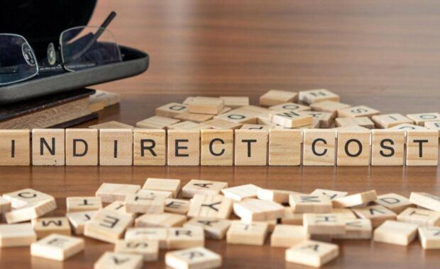 indirect cost word or concept represented by wooden letter tiles on a wooden table with glasses and a book