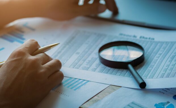 man looking through a magnifying glass to documents