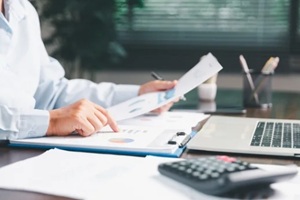 office businesswoman hand to operate calculator analyzing financial data, counting costs on desk