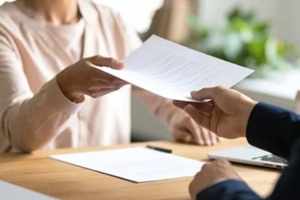 two individuals exchanging documents across a wooden desk symbolizing a business transaction or important discussion
